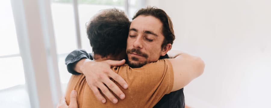 Two men hugging in a bright room, symbolizing emotional support and connection for those managing incontinence
